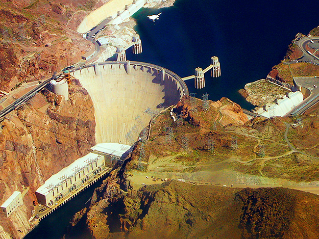Hoover Dam. Big concrete wall separating the river. Water behind dam is higher elevation and much wider than the river below the dam