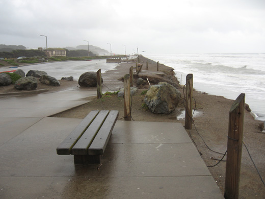 A bench Ocean Beach before after severe erosion. Bench on concrete platform with several feet of ground beyond the platform to the sea.