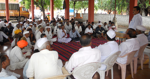 Many men in india dressed in white seated for a meeting