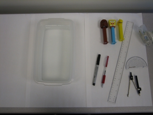 clear container, ruler, compass, protractor, 3 pez dispensers on a table