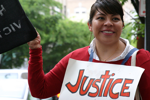 Woman with justice sign around neck and another sign with illegible words in her hand