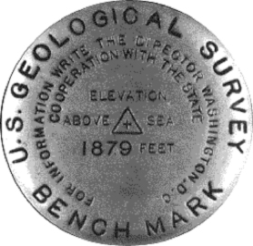 A metal “benchmark” used to mark a location, shows elevation above sea level at +1879 feet.