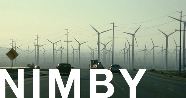 Wind farm as seen from a highway with the word NIMBY written across the bottom