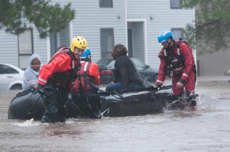 Rescue workers in water up to their knees pulling a boat with people behind them.