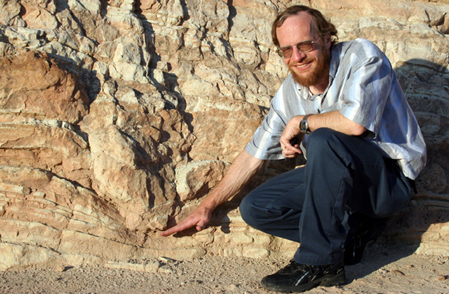 Dr. Alley standing next to an edge-on  dinosaur track.
