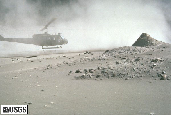 Volcanic ash covering the landscape around the volcano.  A helicopter is hovering near the ground.