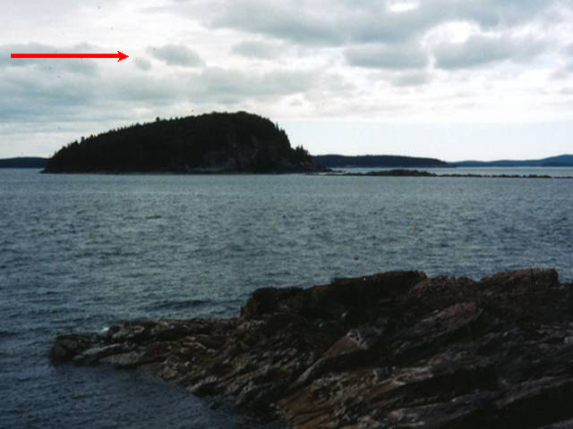 Body of water with island in center. Cloudy skies. Arrow at top left points to the right, indicating direction of ice flow