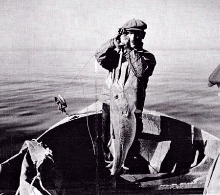 Man in fishing boat holding a moderately large fish.