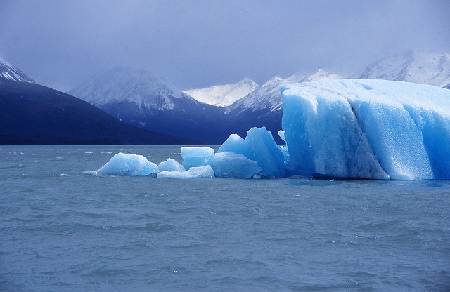 Glacier in a bay surrounded by mountains. Glacier has blue color.
