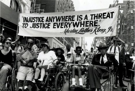 Rally of people in wheel chairs carrying sign "Injustice Anywhere is a Threat to Justice Everywhere" Martin Luther King Jr