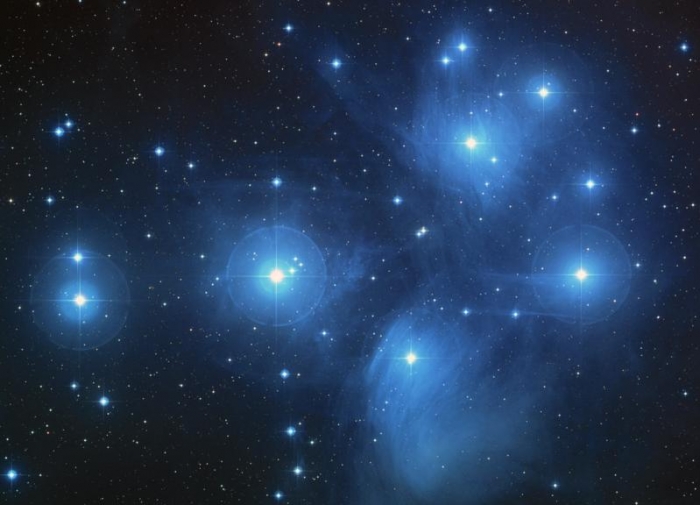 Ground-based telescope image of the Pleiades star cluster, showing the blue reflection nebula surrounding the brightest stars.