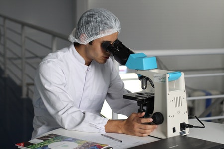 Figure in lab coat and hair net looking through microscope