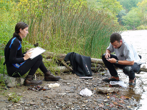 researchers sitting at water's edge writing down observations in notebook