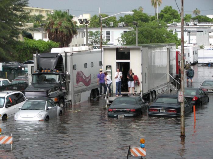 Image of film crew standing on trailers edge with water coming up past the wheels of the cars.