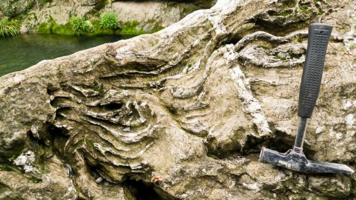Raised swirl formations in a rock with a hammer sitting next to it. 