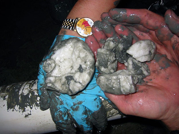 Hands holding clumps of gas hydrate, white but covered with wet sand.