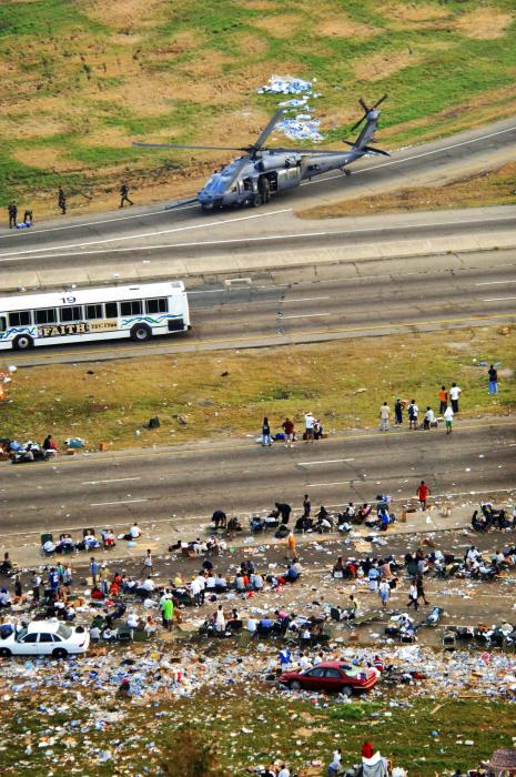 Debris-strewn highway with people, bus, and helicopter.