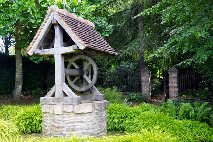 Groundwater extraction well  in the Garden of Cambremer, France. Cute stone hut with wheel and rope 