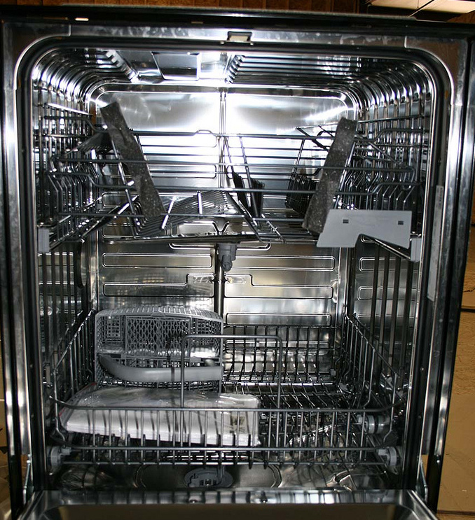 Inside of a dishwasher showing upper rack, spray arm, lower rack, door gasket, and detergent dispenser