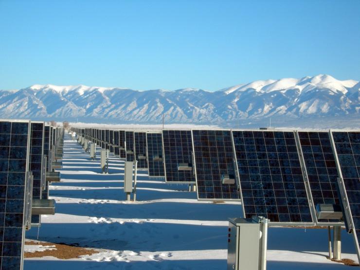 solar panels on snow covered ground with mountains behind them.