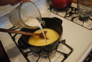 Corn starch mixed with water is being poured into a sauce mixture on a stove
