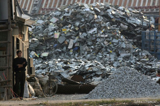 photograph of a man standing before a very large pile of electronic waste.