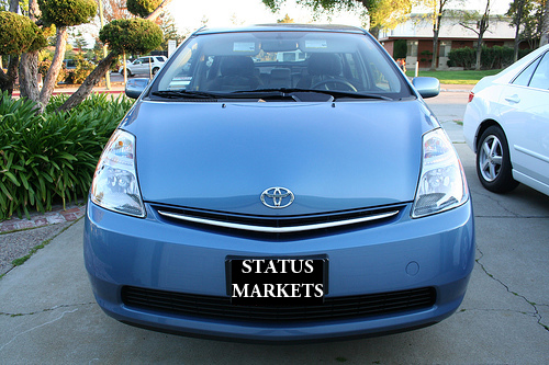  blue Toyota Prius with the words "status markets" photo shopped onto the front license plate 