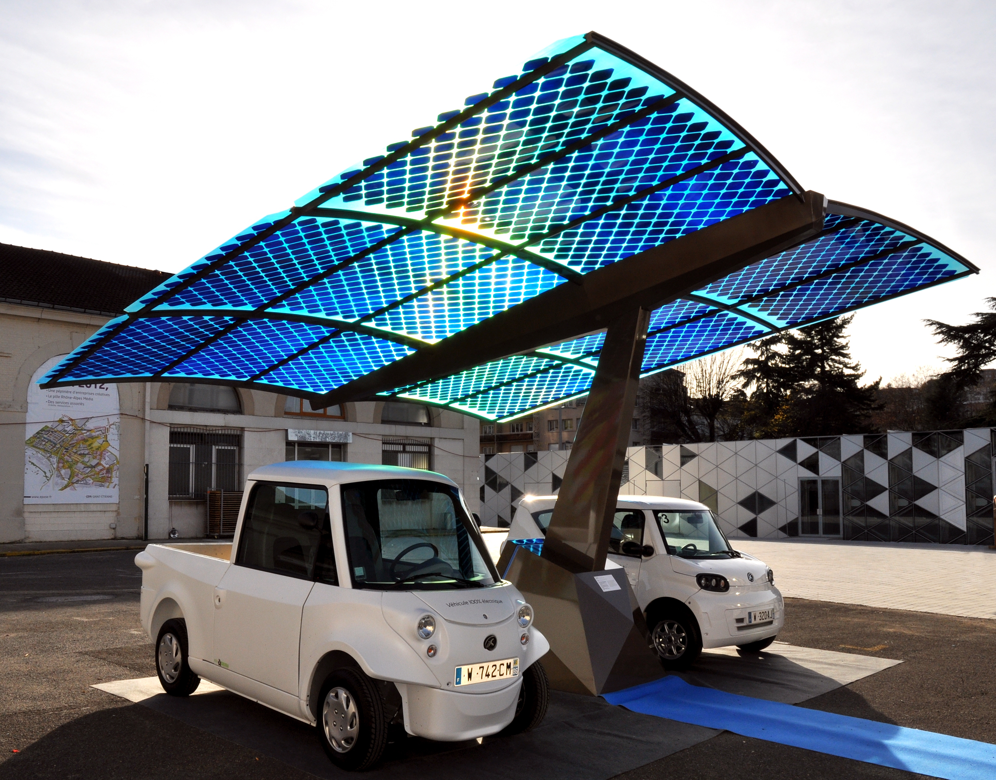 2 electric vehicles sitting under blue Photovoltaic shading structure. Described in caption.