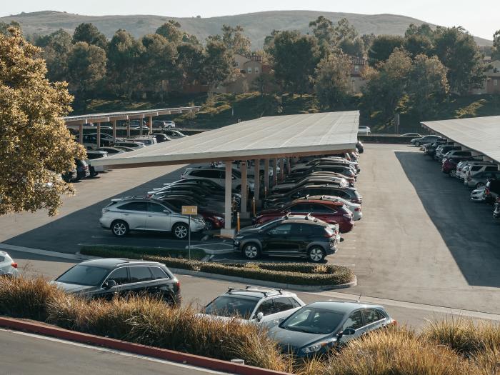 Solar panels in a parking lot, cars are parked underneath.