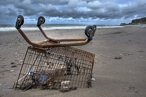 rusty shopping cart turned upside down with trash under it on the beach