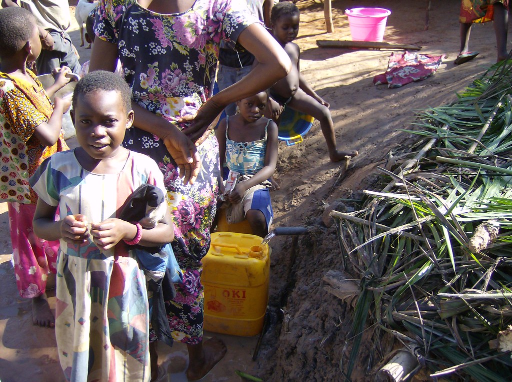 image showing a group of children around a drinking water pipe filling old plastic buckets