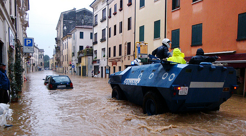 Image of the flooding in a city with a car underwater in the street. Armored and raised police vehicle drive through water