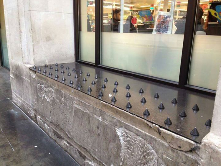 The image shows the exterior of a store window. The sill is made of concrete; a metal plate covered in short, thick spikes has been affixed to the sill and runs its entire length.