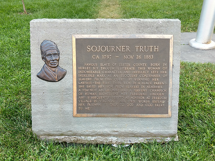 The image shows a rectangular stone monument. On it is a bronze relief bust of Sojourner Truth, and to the right of that is a plaque detailing her historical significance.