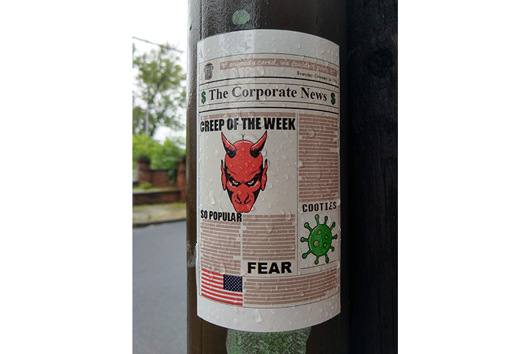 The image shows a sticker attached to a lamppost. The sticker is made to look like a newspaper called “The Corporate News.” The lead story is titled “Creep of the Week” and features a stylized portrait of a head of a person with red skin, pointed ears, and two horns, with the caption “So Popular.” A second story is headlined “Cooties” and shows a green, stylized COVID-19 particle. A third headline reads, simply, “Fear.”