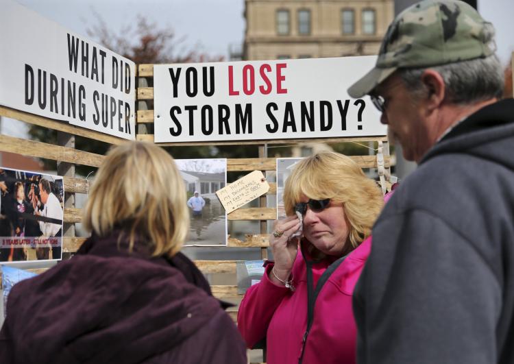 A woman crying in front of a sign that says "What did you lose during super storm sandy?