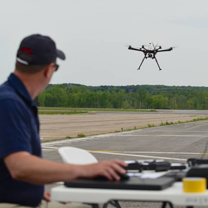 man standing on runway navigating a drone which is flying towards him.