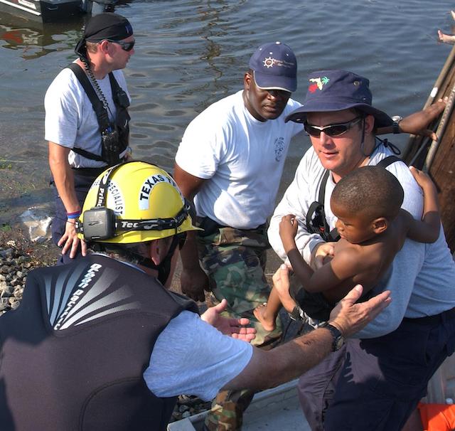 Responders transporting a small child to safety as they hand a child into a boat.