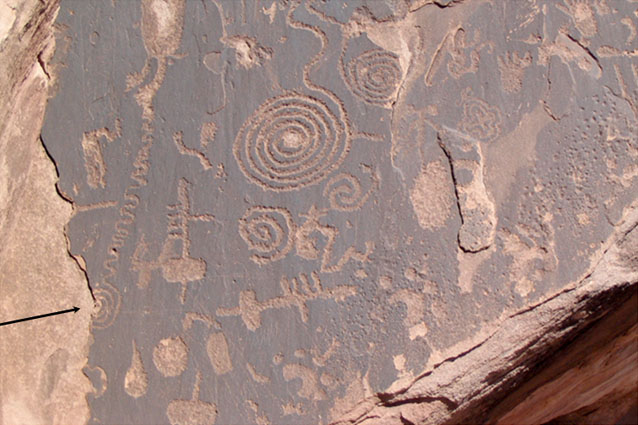 Ancestral Puebloan rock carving showing surface flaking. Arrow points to half-spiral. Petrified Forest National Park