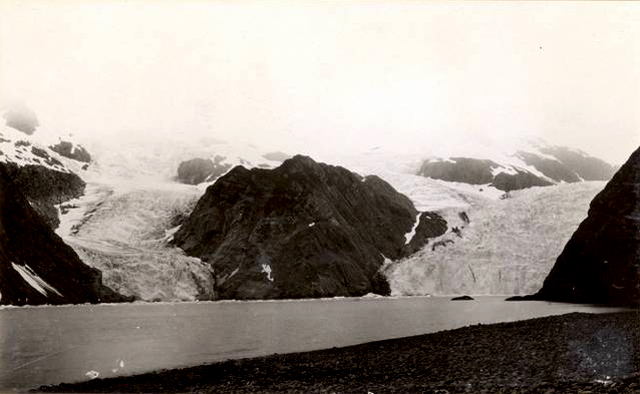 Holgate Glacier, AK, 1909. Glacier covers much of rock, water in foreground.