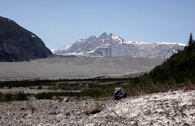 McCarty Glacier, AK, 2004. Rocks in foreground, no water, melting glacier in background in front of snow capped mountains.