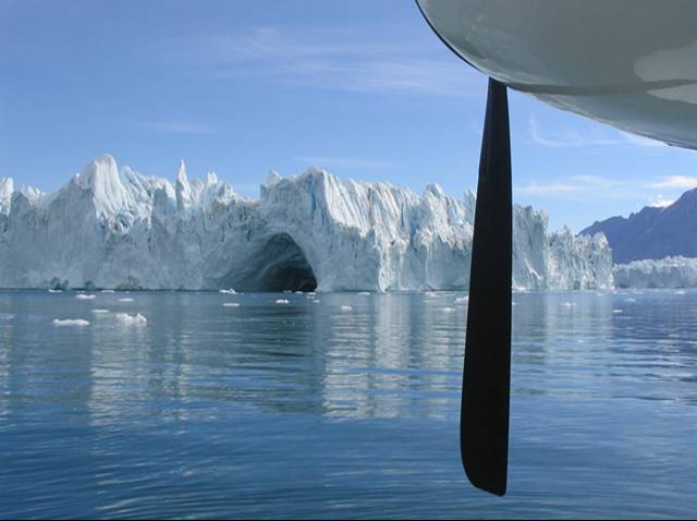 Northwest Fjord, east Greenland.  Iceberg under blue sky and surrounded by blue water. Float-plane propeller right foreground.