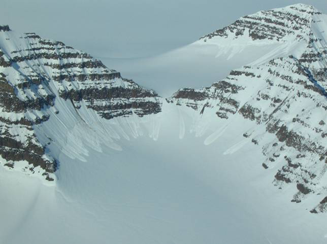 Several small snow avalanches into a cirque surrounded by layered rock peaks, east Greenland.