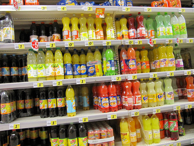 Shelves in a store with carbonated beverages in cans and plastic, glass bottles.