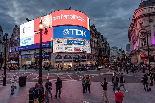 Picadilly circus in London. Road junction with a building featuring large curved screens on the corner