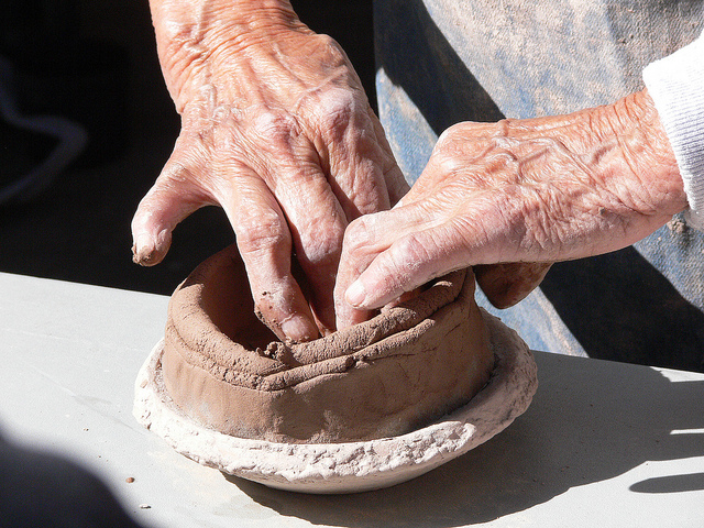 Hands shaping a clay pot made out of coils