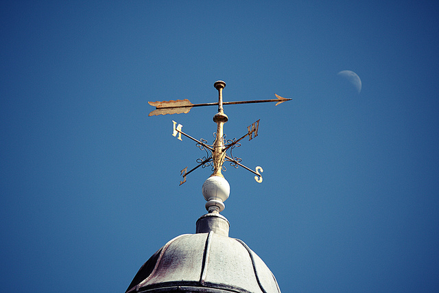 weathervane on top of building with moon and blue sky behind