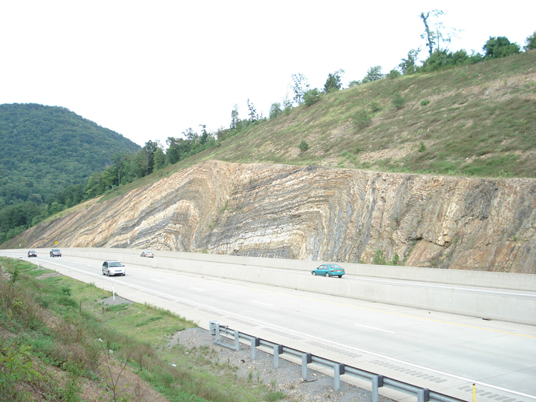 picture of a road cut of exposed rock strata showing layering and folding